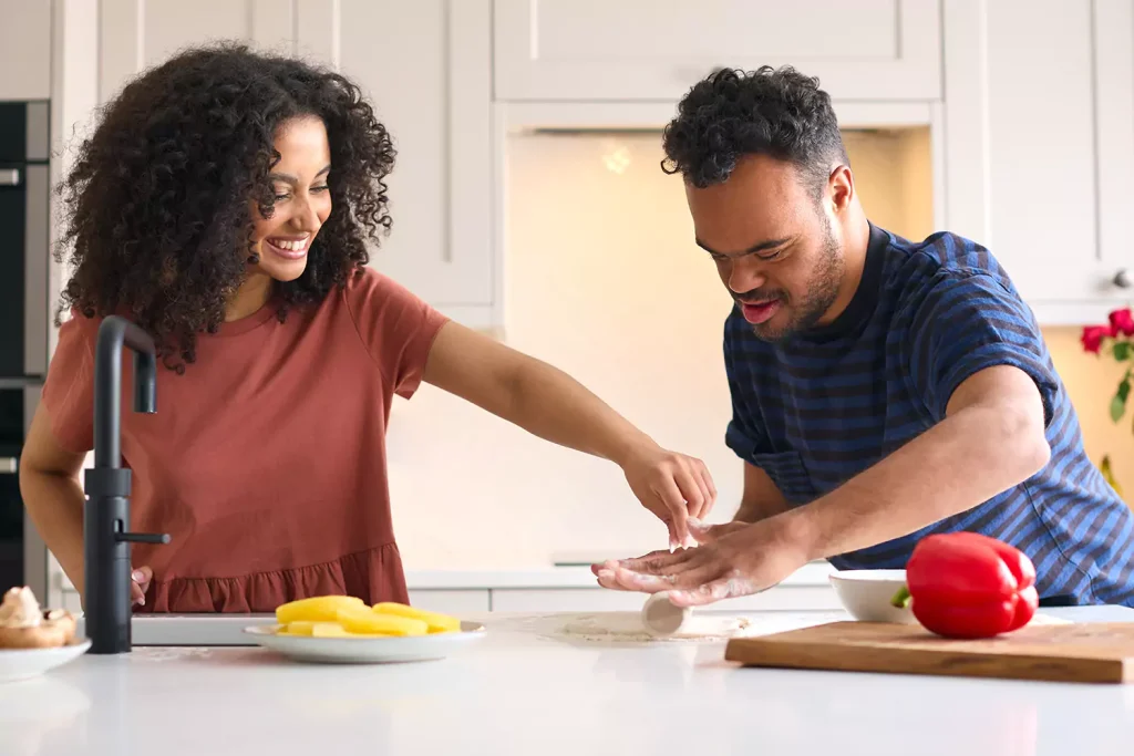 A down syndrome man and his care giver are having fun while cooking pizza