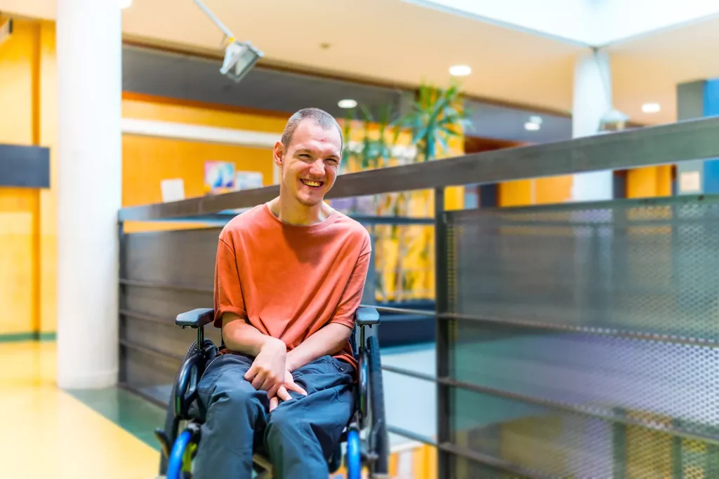 A young disabled man in a wheelchair is smiling at the camera