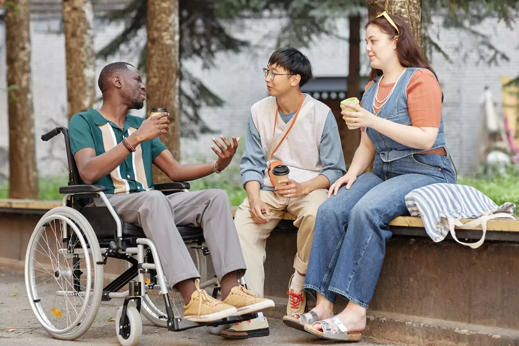 A group of friends are enjoying a coffee together while outdoors. One of the friends is sitting in a wheelchair.
